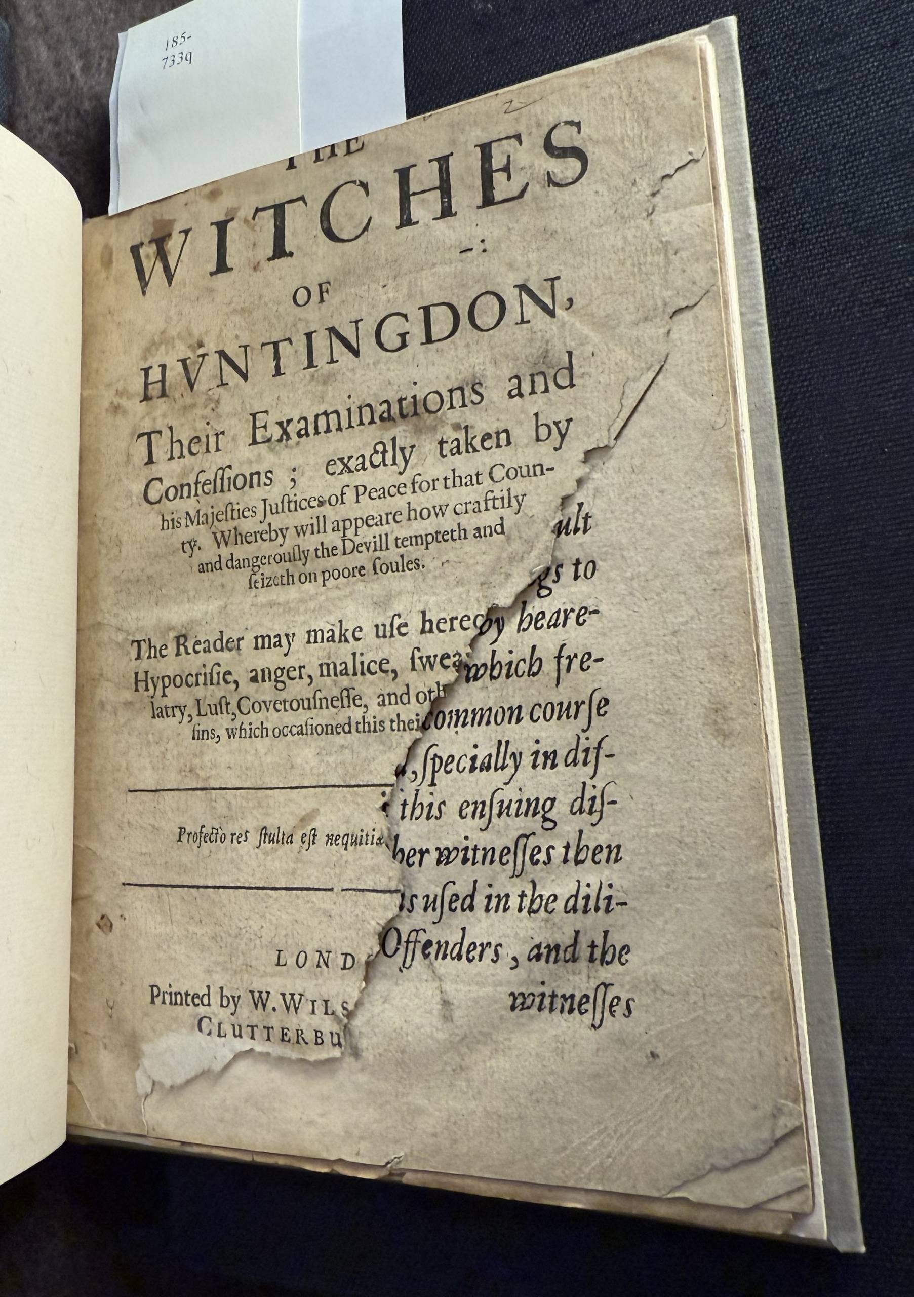 A printed title page of a book that is missing a large triangle shaped part of the bottom right of the page, revealing the text page of printed text underneath.