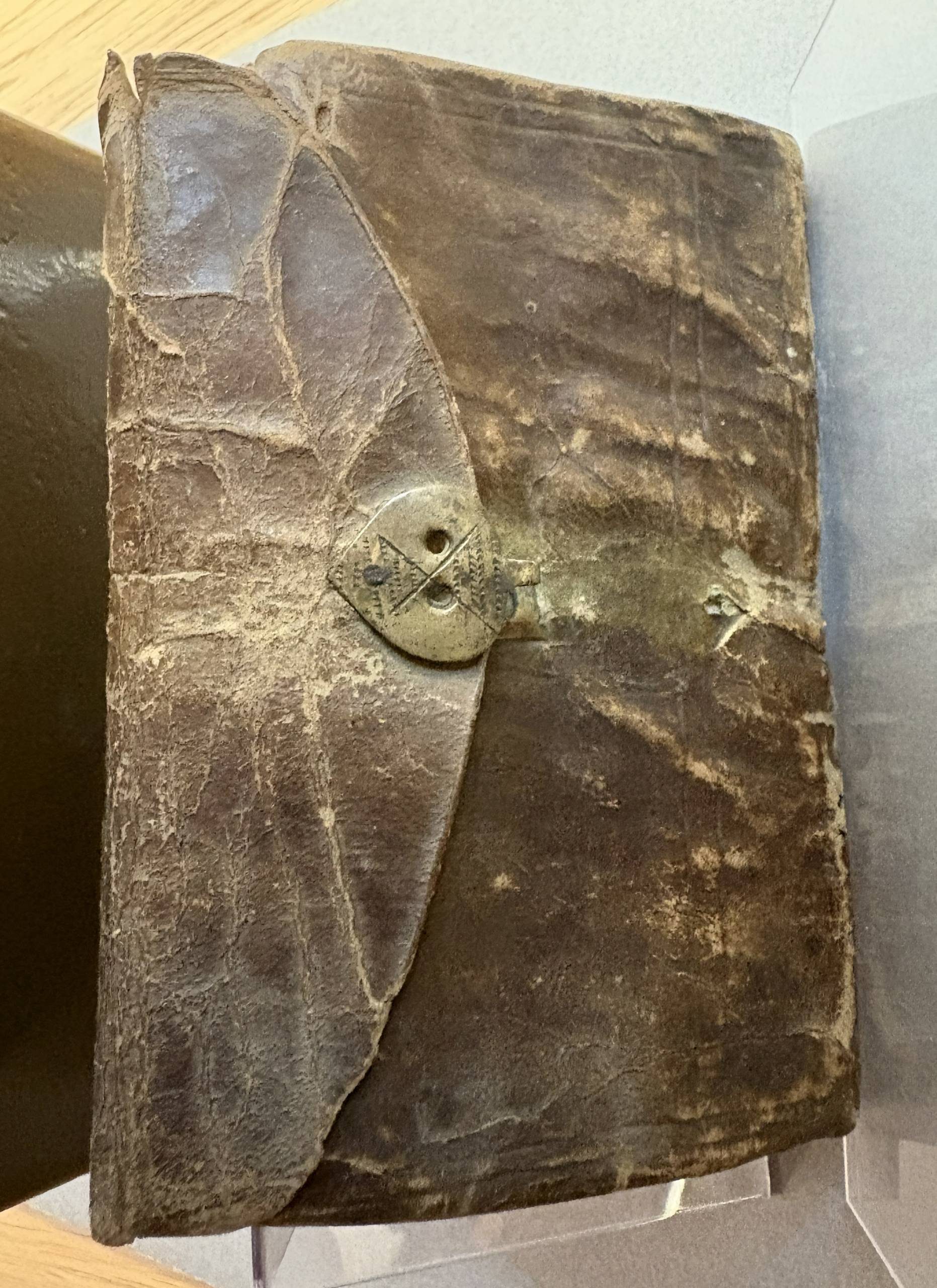 A closed book with a weathered vellum cover and an almost heart-shaped metal clasp.