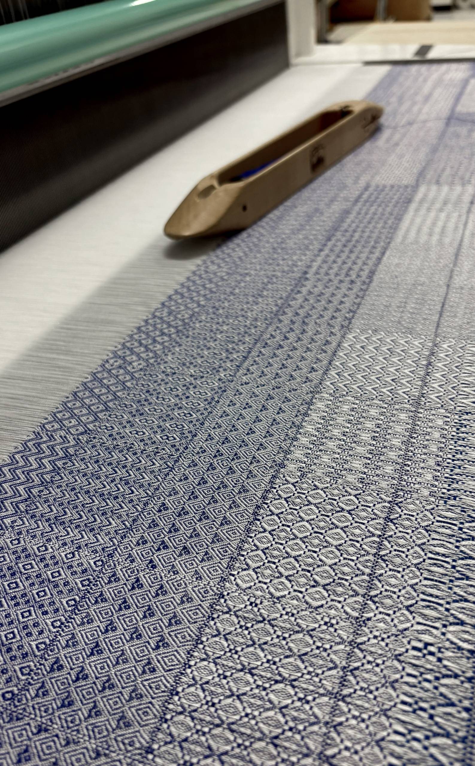 A stretch of cloth with a variety of blue patterns, with a loom shuttle resting on top of it.