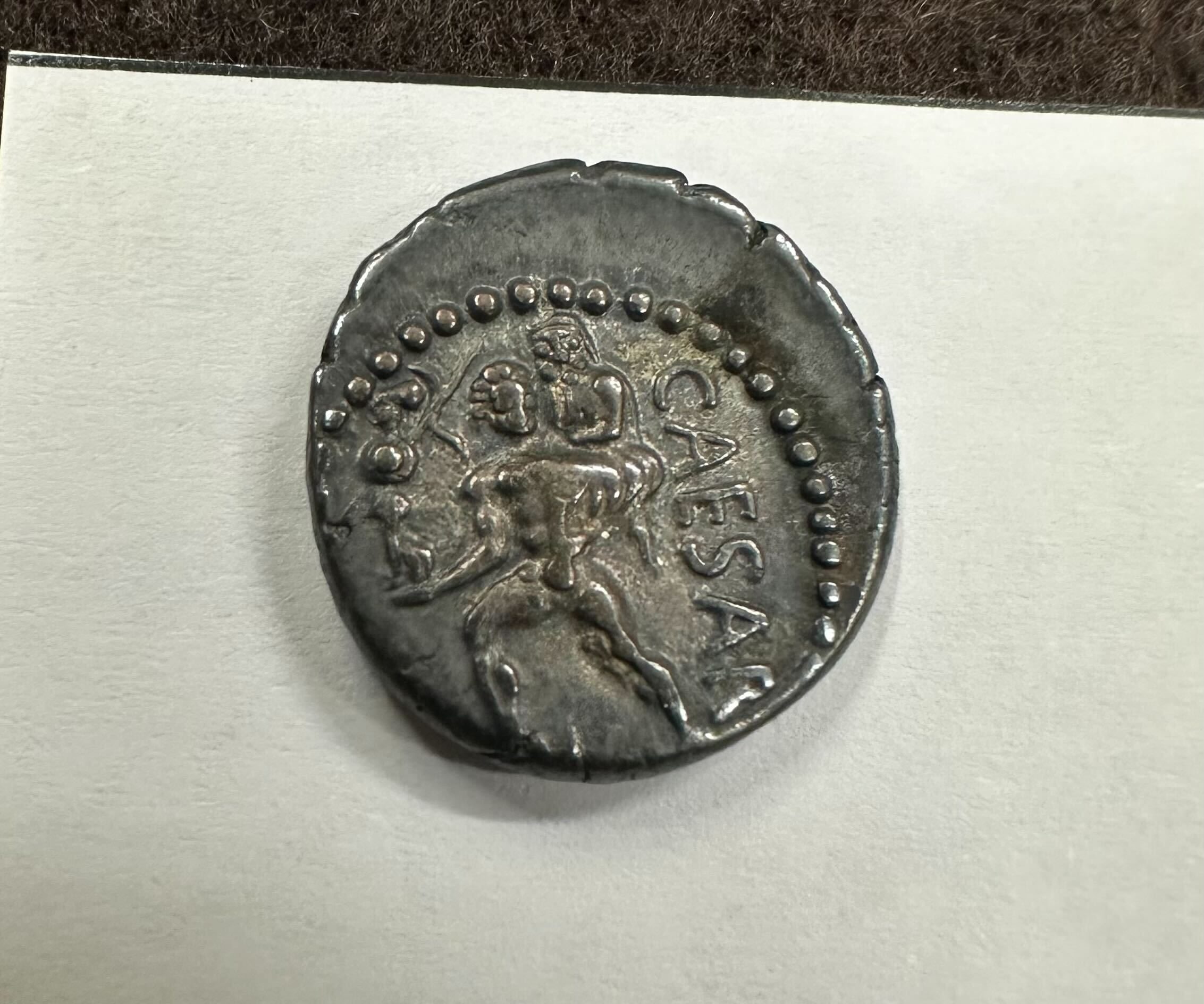 A silver coin showing a man carrying another man with the word CAESAR written alongside the figures.