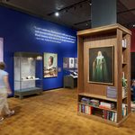 Striking portrait photographs hang on the walls next to glass exhibition cases and against wooden bookshelves
