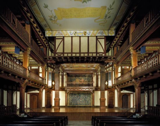 An interior of a square Elizabethan theatre with a colorful ceiling and curtain