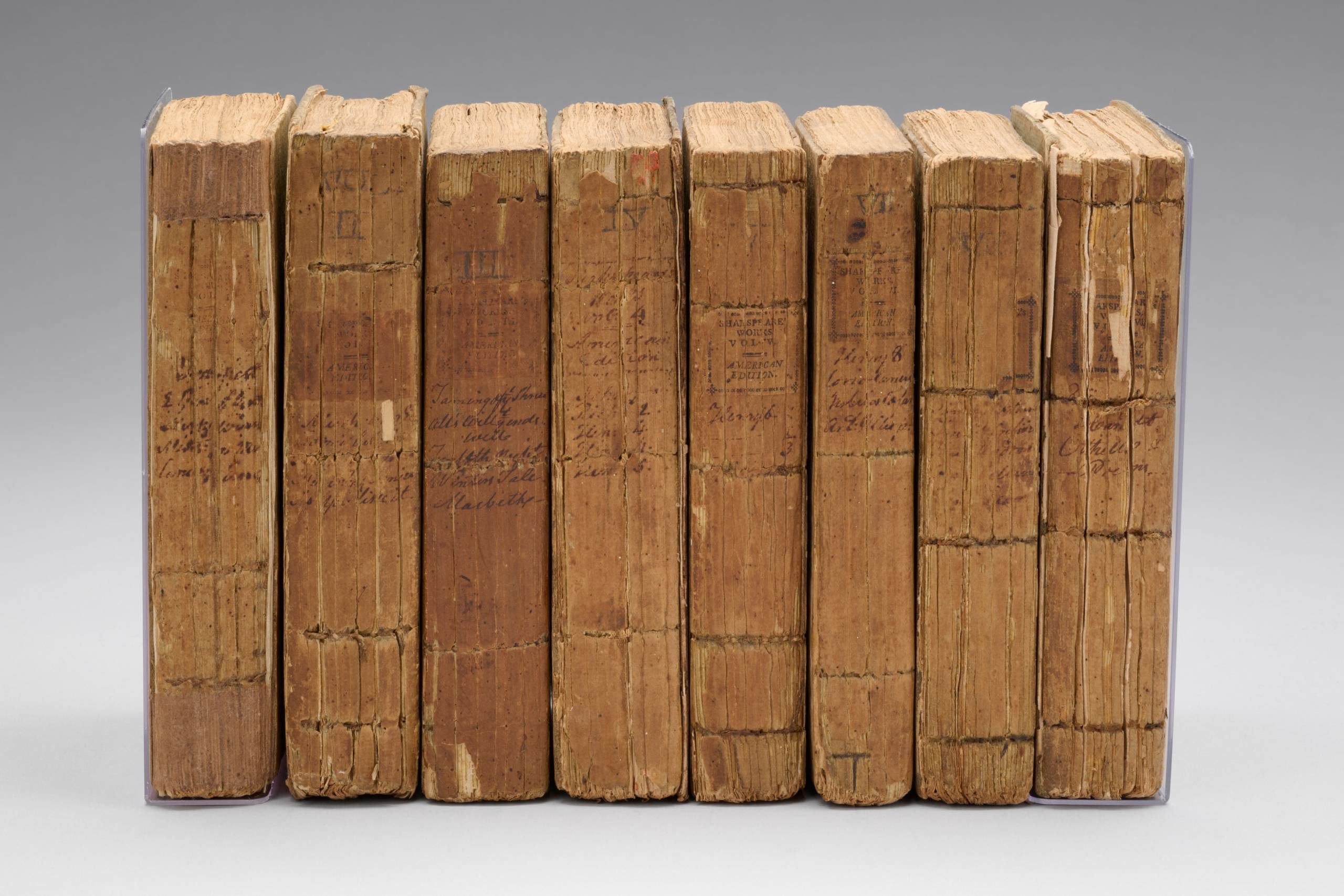 A set of eight upright books with cracked spines and handwritten titles facing outwards.