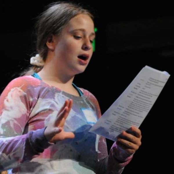 Girl standing on stage reading from a paper.