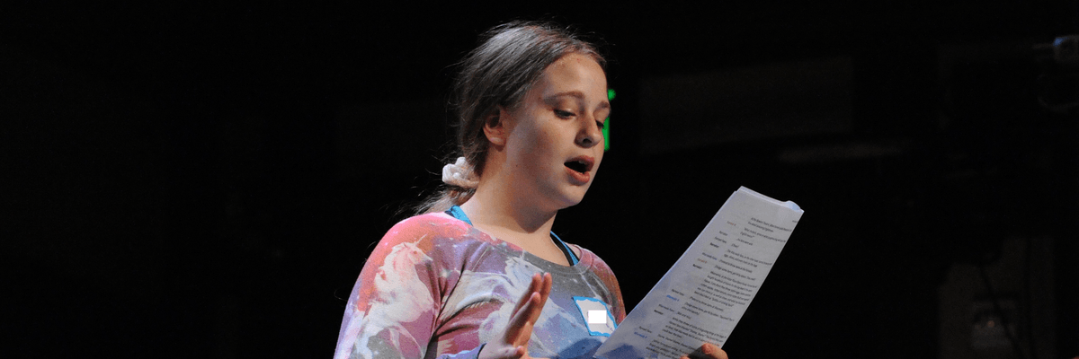 Girl standing on stage reading from a paper.