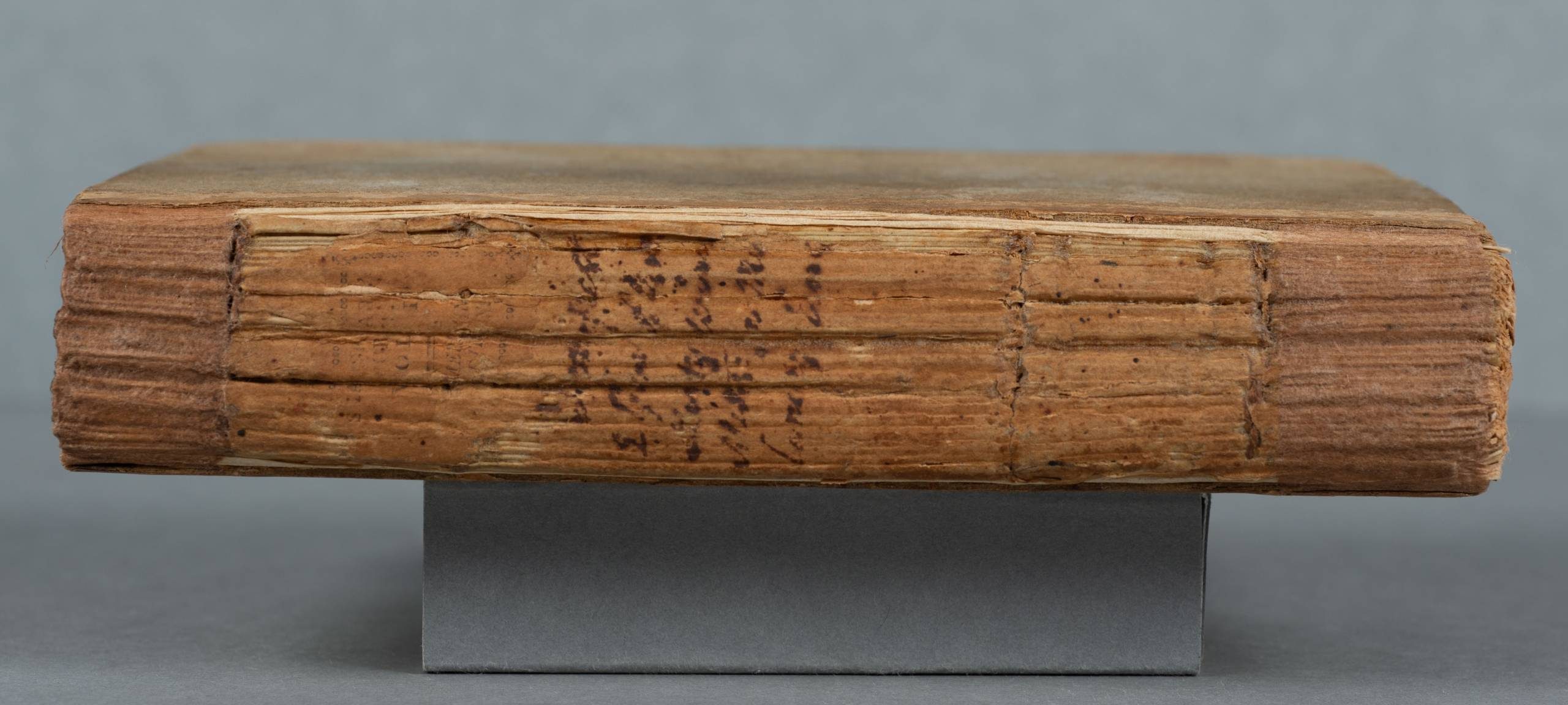 A closed book lying on its side on a gray block. The spine is furrowed and there is a handwritten title that is not legible in the photo.