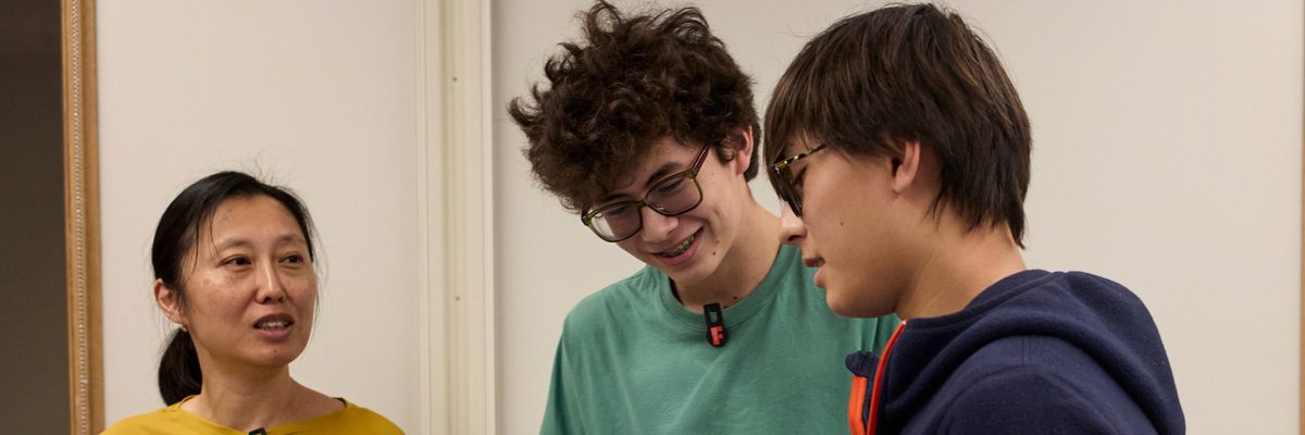 Two boys and a woman reading out loud