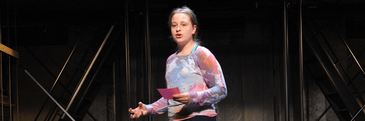 A girl standing on a theater stage talking out loud