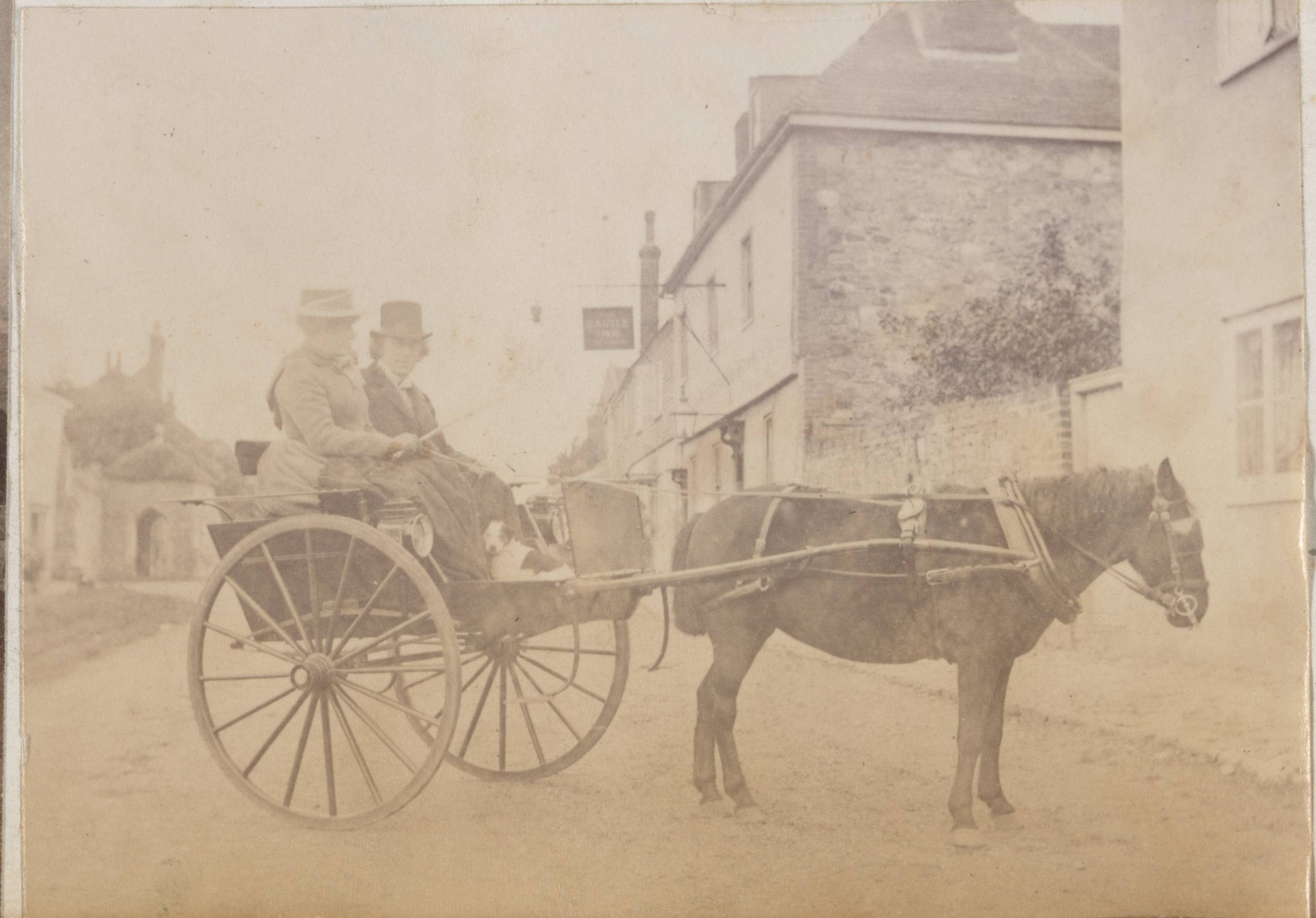A faded sepia-toned photograph of two people in a gig hitched to a small, dark horse.
