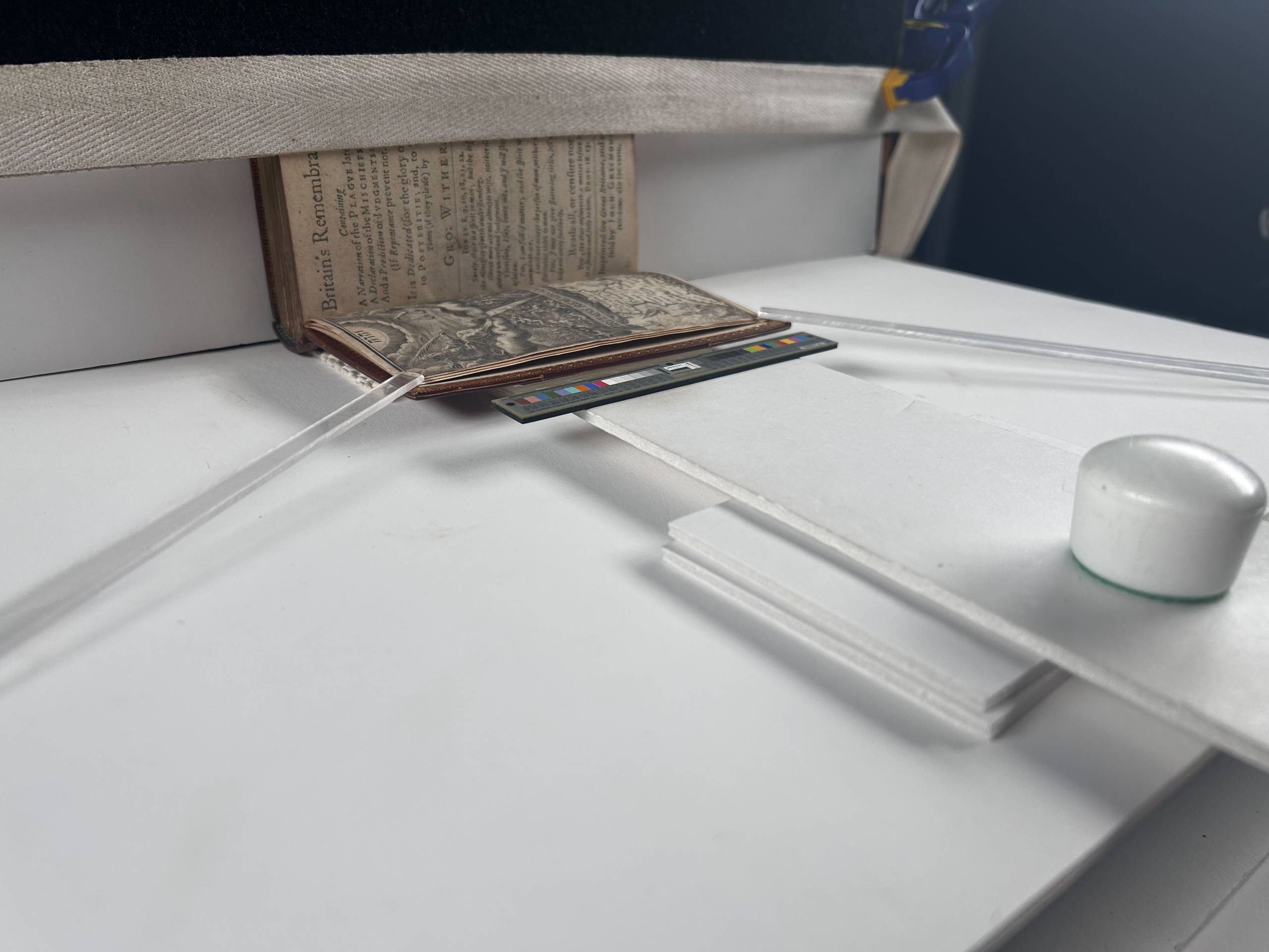 A distance shot of the imaging supports showing a book propped open and the page held down by clear plastic supports.
